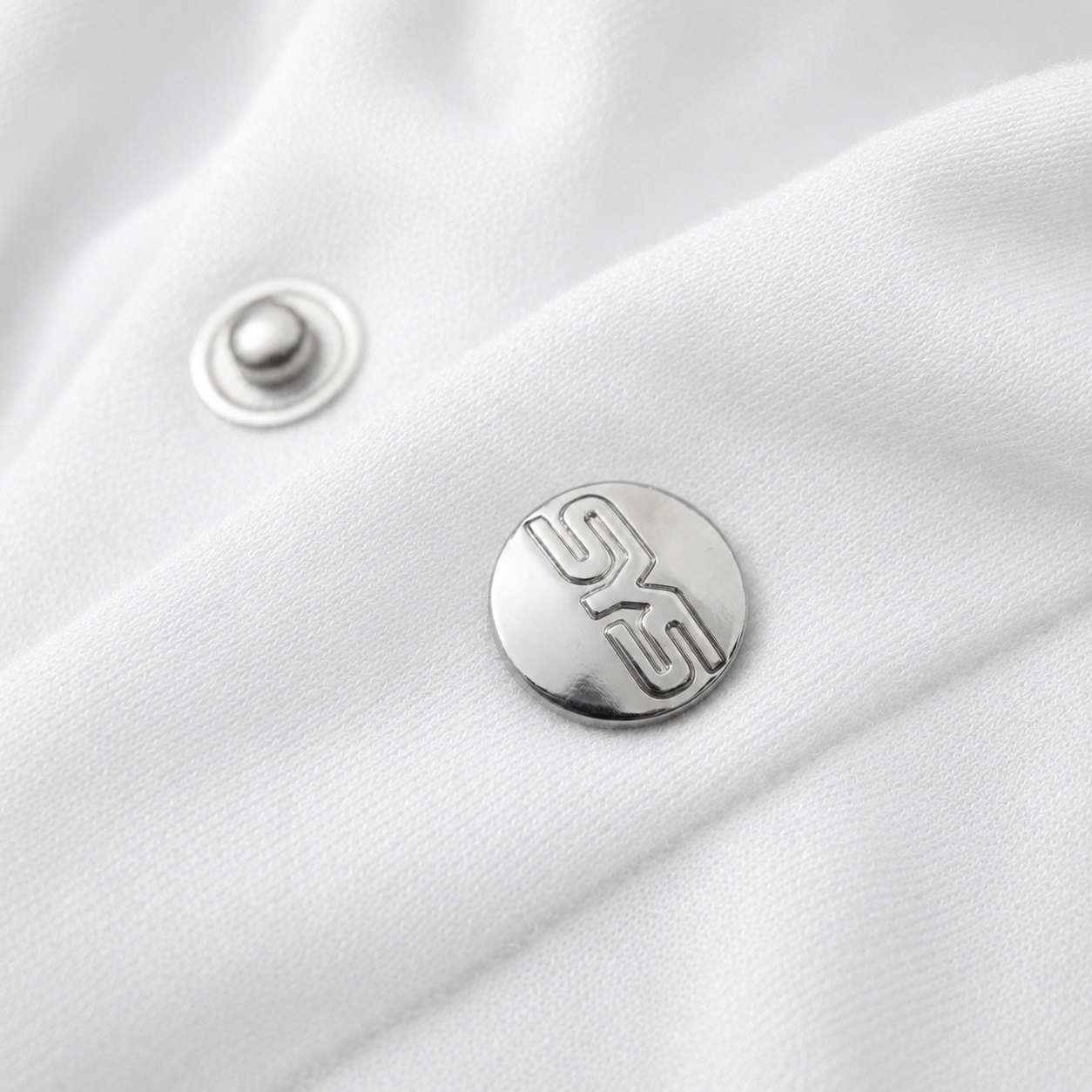 Close-up of a silver button with a logo on a white fabric background