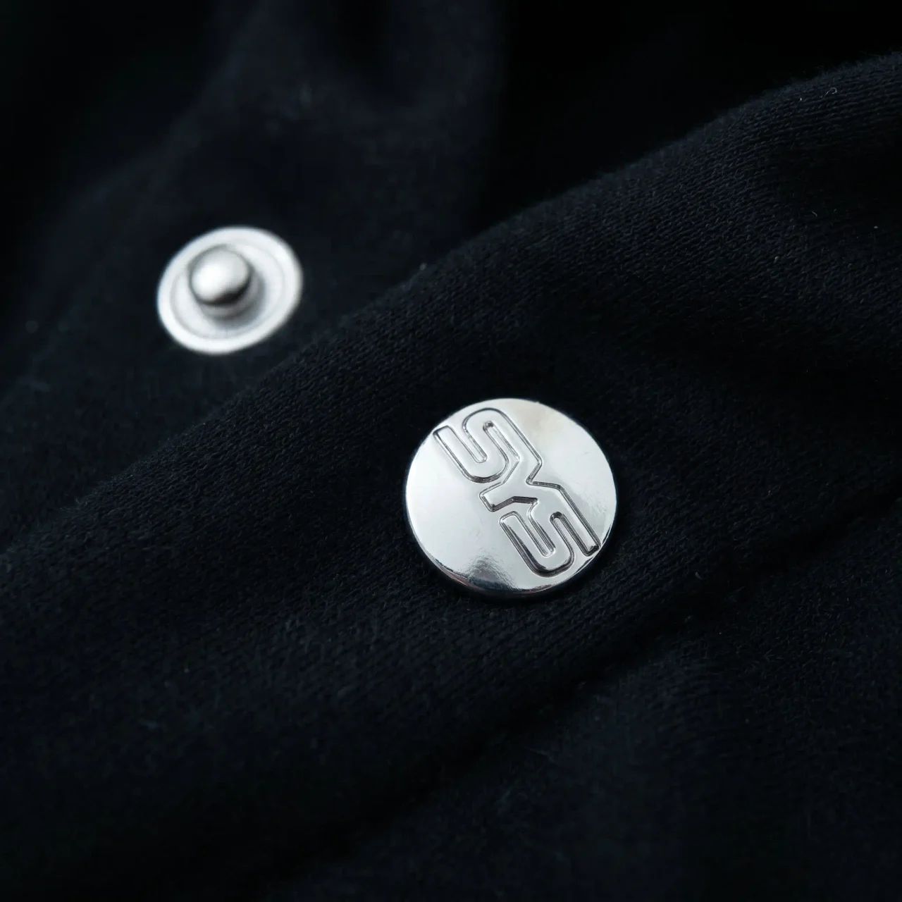 Close-up of a black fabric surface with silver buttons featuring a logo.