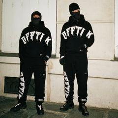 Two people wearing matching black outfits with 'OFFTIK' branding in an urban setting.