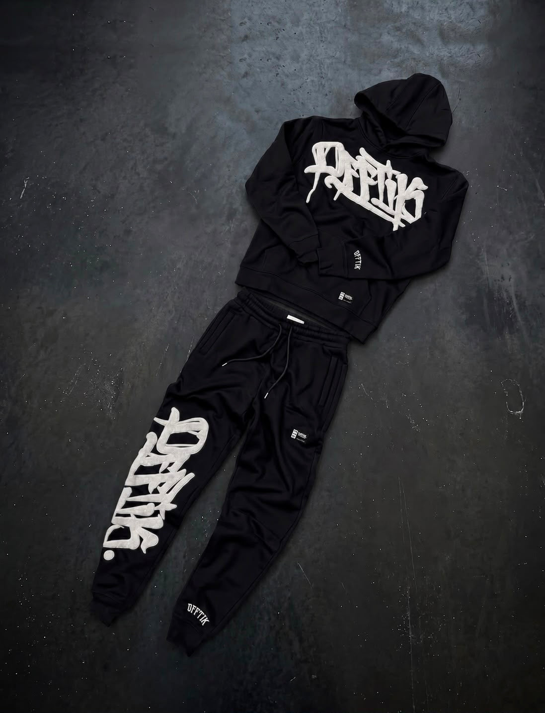 Black hoodie and pants set with white branding on a dark surface
