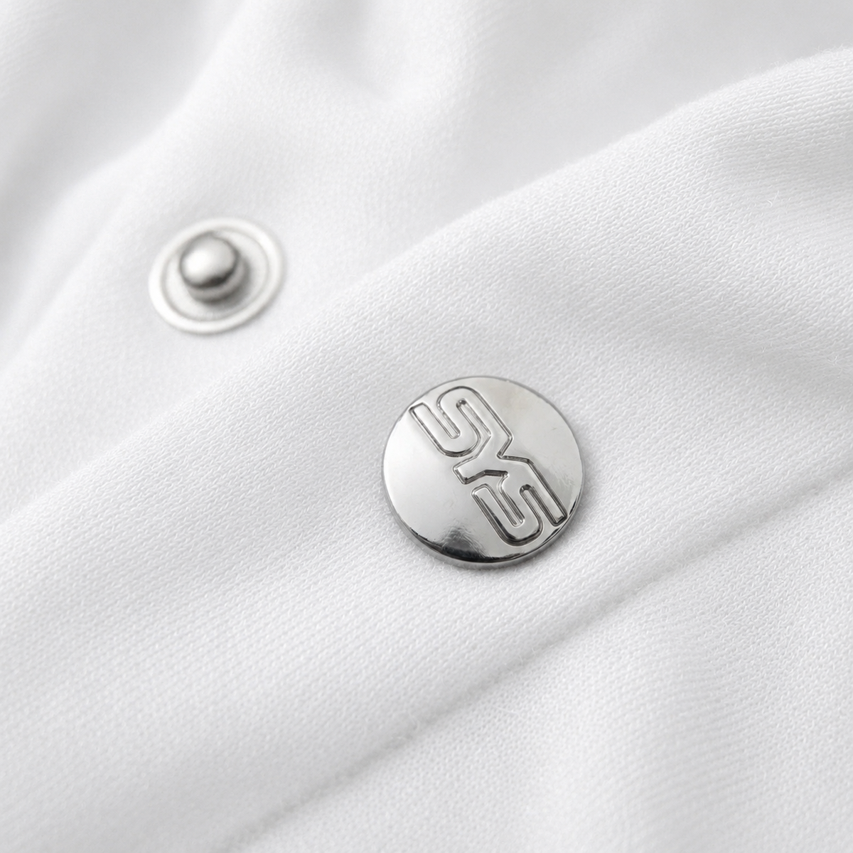 Close-up of a silver button with a logo on a white fabric background, image 4