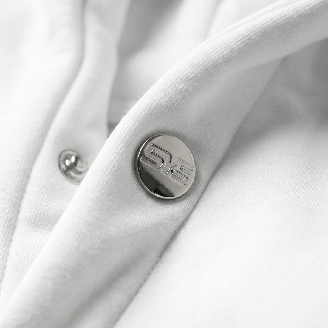 Close-up of a white garment with a button featuring a logo on a white background, image 5
