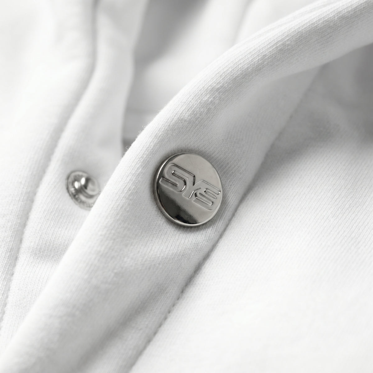 Close-up of a white garment with a button featuring a logo on a white background, image 5