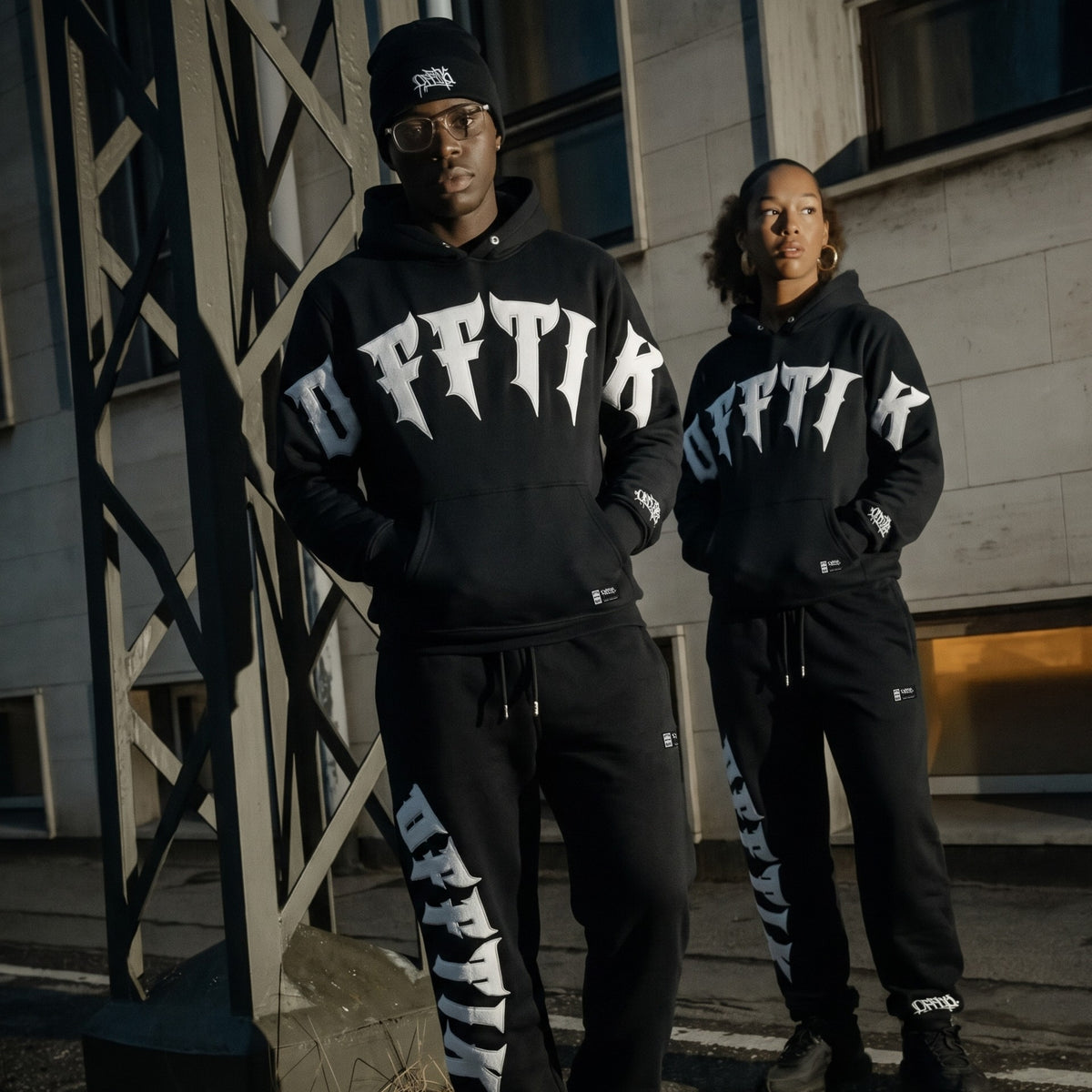 Two people wearing matching black hoodies with white text in an urban setting., image 3
