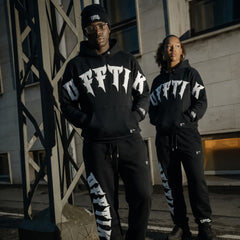 Two people wearing matching black hoodies with white text in an urban setting.