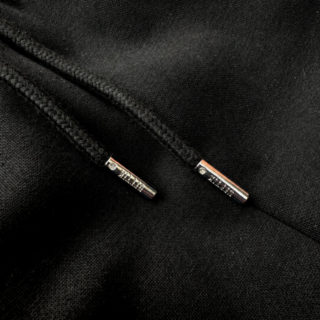 Close-up of black drawstring with metal tags on a black fabric background, image 6