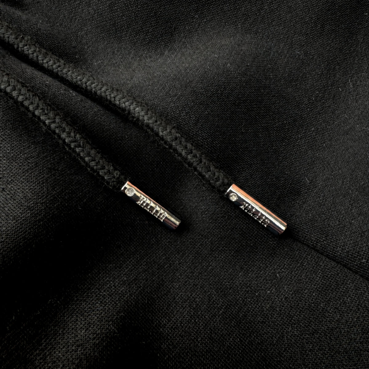 Close-up of black drawstring with metal tags on a black fabric background, image 6