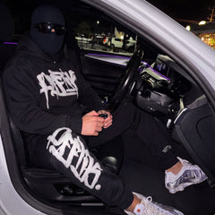 Person wearing a black hoodie with white text sitting inside a car at night.