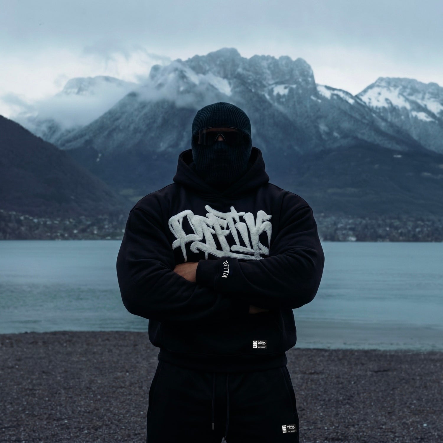 Person wearing a black hoodie with white text in front of a mountainous landscape