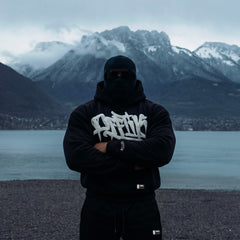 Person wearing a black hoodie with white text in front of a mountainous landscape