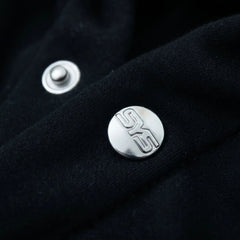 Close-up of a black fabric surface with silver buttons featuring a logo.