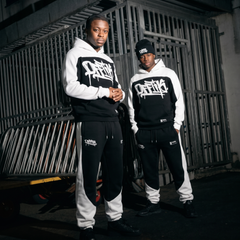 Two individuals wearing matching black and white tracksuits with a logo in an urban setting.